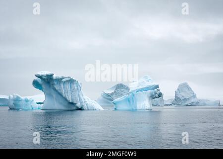 Eisberge, jeder ganz individuell, wie handgefertigte Eisskulpturen, schweben leise über das Meer der Antarktis. Stockfoto