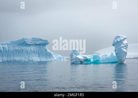 Eisberge, jeder ganz individuell, wie handgefertigte Eisskulpturen, schweben leise über das Meer der Antarktis. Stockfoto