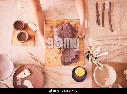 Töpferfrau und Hände mit Sicht von oben auf Ton am Tisch mit Werkzeugen für Produktion und Fertigung. Bildhauerprozess und handgefertigte Keramikwerkstatt von Stockfoto