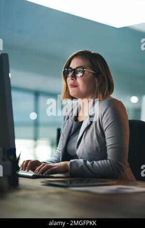 Der Erfolg kann bei Bedarf lange Stunden aushalten. Eine junge Geschäftsfrau, die lange an einem Computer in einem Büro arbeitet. Stockfoto