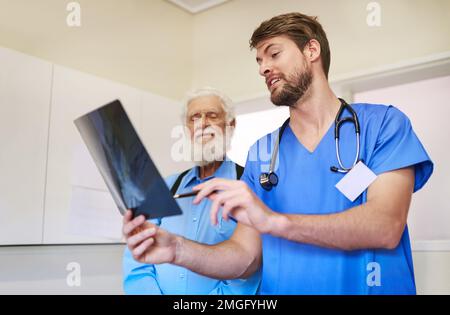Sieh mal, was ich auf deinem Röntgenbild gefunden habe. Ein junger Arzt und sein Seniorpatient schauen sich gemeinsam ein Röntgenbild an. Stockfoto
