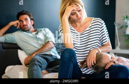 Müde Mutter und Vater, die auf der Couch sitzen, fühlen sich genervt, erschöpft, stressig mit dem kleinen Mädchen. Stockfoto