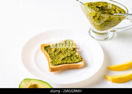 Toast mit Avocado und Chimichurri-Sauce auf einem weißen Teller. Gesundes vegetarisches Essen. Weißer Hintergrund. Stockfoto