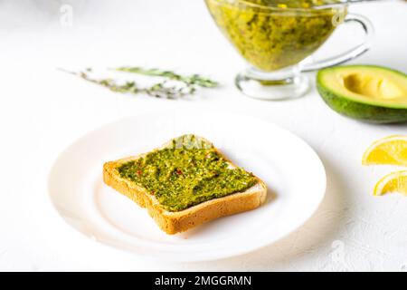 Toast mit Avocado und Chimichurri-Sauce auf einem weißen Teller. Gesundes vegetarisches Essen. Weißer Hintergrund. Stockfoto