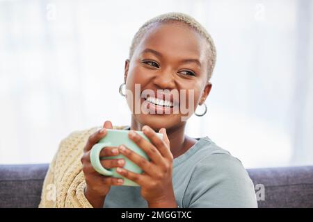 Schwarze Frau, entspann dich und entspann dich mit einem Drink, Kaffee und einem Lächeln im Wohnzimmer für meine Zeit. Junge afrikanische Dame, Frieden oder Tee auf der Couch für Glück Stockfoto