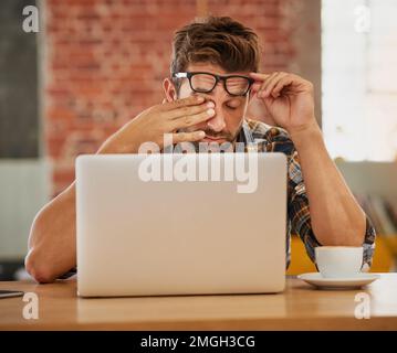 Sie kämpfen darum, inspiriert zu bleiben. Ein erschöpfter junger Unternehmer, der an seinem Laptop in einem Café arbeitet. Stockfoto