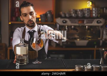 Der Barkeeper gießt das Getränk aus dem Messbecher in ein mit Eiswürfeln gefülltes Cocktailglas. Stockfoto