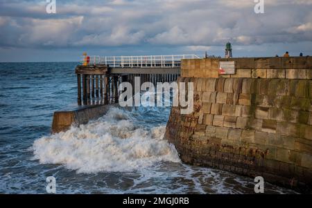 Große Wellen stürzen sich durch die Hafeneingangspiers in Whitby, North Yorkshire, Großbritannien Stockfoto