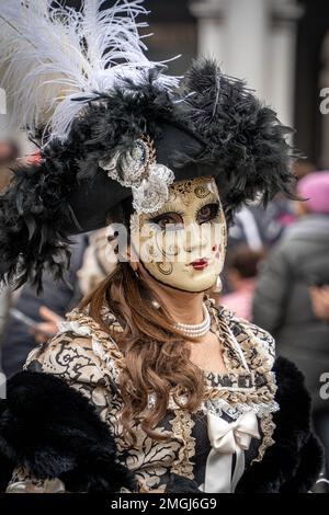 Eine Frau in einem dunklen mittelalterlichen Kostüm, einer weiblichen Karnevalsmaske und einem großen schicken Hut mit Federn auf dem Karneval in Venedig, Italien Stockfoto