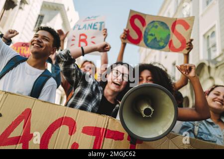 Eine Gruppe lebhafter Klimaschutzaktivisten, die mit Bannern und einem Megafon protestieren. Glückliche junge Menschen, die gegen die globale Erwärmung und Umweltverschmutzung marschieren. Multieth Stockfoto