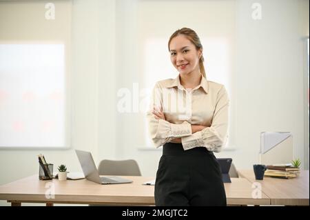 Professionelle und erfolgreiche asiatische Geschäftsfrau oder Chefin der Millennials steht in ihrem Büro mit überkreuzten Armen. Stockfoto