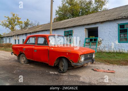 Ein zerstörtes ziviles Auto steht in der Nähe eines zerstörten Hauses. An der Karosserie des Autos befinden sich Löcher von Kugeln und Splittern. Russische Invasion der Ukraine Stockfoto