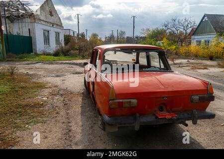 Ein zerstörtes ziviles Auto steht in der Nähe eines zerstörten Hauses. An der Karosserie des Autos befinden sich Löcher von Kugeln und Splittern. Russische Invasion der Ukraine Stockfoto