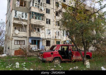 Ein zerstörtes ziviles Auto steht in der Nähe eines zerstörten Hauses. An der Karosserie des Autos befinden sich Löcher von Kugeln und Splittern. Russische Invasion der Ukraine Stockfoto