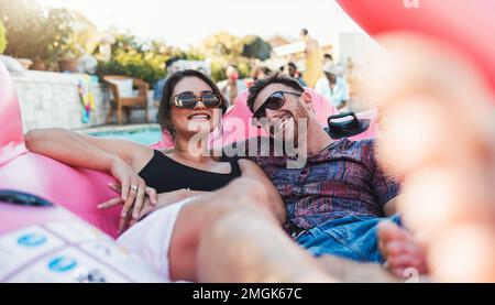 Paare, entspannen und lächeln für eine Poolparty auf einem aufblasbaren Floß im Wasser und genießen den Sommerurlaub zusammen. Glücklicher Mann und glückliche Frau beim Schwimmen Stockfoto