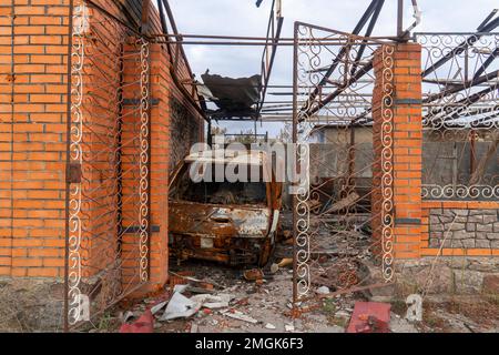 Auf Dem Land. Zerstörtes, ausgebranntes Zivilauto steht auf dem Hof eines zerstörten Hauses. Krieg in der Ukraine. Russische Invasion der Ukraine. Kriegsverbrechen Stockfoto