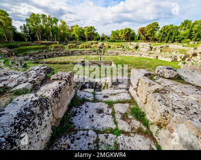 Römisches Amphitheater von Syrakus - I Cent. AD - III Cent. AD - Archäologischer Park Neapolis - Syrakus, Sizilien, Italien das Amphitheater hat zwei Eingänge und wird durch ein komplexes Treppensystem bedient, das von der oberen Ebene absteigt, die sich draußen befindet. Die Arena war im Zentrum mit einem großen rechteckigen Raum ausgestattet, der ursprünglich bedeckt war und über eine unterirdische Passage mit dem südlichen Ende des Denkmals verbunden war, auf der Achse des Eingangskorridors. Rund um die Arena zeichnet sich die Cavea durch ein hohes Podium aus, hinter dem ein überdachter Korridor mit Toren für den Zugang zur Arena für Gladiatoren A verläuft Stockfoto