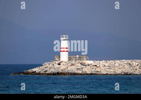 Leuchtturm Turm auf einem Steinsteg in azurblauem Meer gegen Neblige Berge Stockfoto