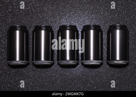 Leere schwarze Aluminiumdosen in einer Reihe auf schwarzem Hintergrund mit Funkeln bei hartem Licht Stockfoto