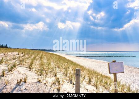 Die Sonne scheint durch dicke Wolken am Ostseestrand. Schild am Strandübergang. Groynes an der Küste. Sandstrand in Zingst. Landsca Stockfoto