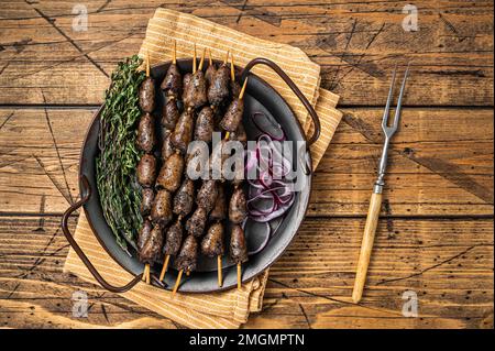 Brasilianisches Barbecue von Churrasco, Hühnerherzen, gegrillte Kebabs mit Kräutern und Gemüse. Holzhintergrund. Draufsicht Stockfoto