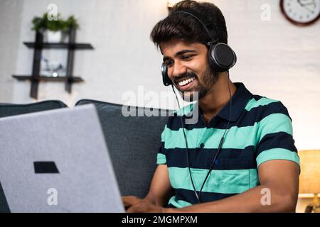 Fröhlich lächelnder junger Mann mit Kopfhörern, der lacht, während er einen Comedy-Film auf dem Laptop abspielt - Konzept von Freizeitaktivitäten, Entspannung und Selbstpflege Stockfoto