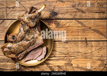 Gebackenes ganzes Lammschulterbein mit Kräutern und Gewürzen auf einer Stahlplatte. Holzhintergrund. Draufsicht. Speicherplatz kopieren Stockfoto