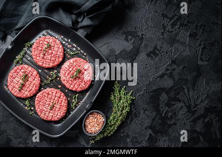 Rohes Rinderfleisch Burger Steak Koteletts in Grillpfanne bereit zum Kochen. Schwarzer Hintergrund. Draufsicht. Speicherplatz kopieren Stockfoto