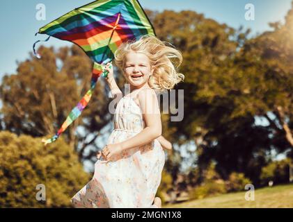 Drachen, Laufen und Mädchen laufen in einem Outdoor-Park mit Sommerspaß und Lächeln. Natur, Kinderurlaub und Glück der Kinder in der Sonne mit Freiheit und Stockfoto