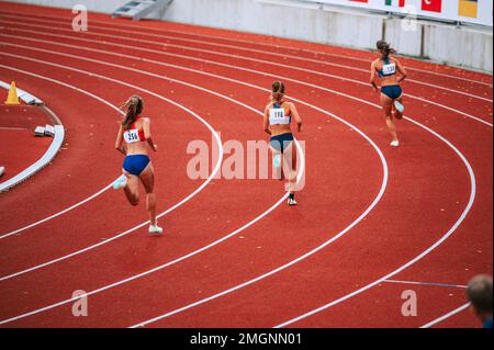 Sportlerinnen an der Startlinie eines 400m-km-Rennens auf der Rennstrecke, die ihre Konzentration und Entschlossenheit bei der Vorbereitung auf den Wettkampf demonstrieren Stockfoto