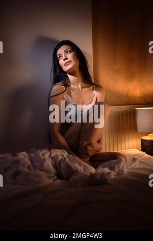 Eine junge, attraktive, dunkelhaarige Frau in ihrem Schlafzimmer, nachts, tief im Gedächtnis Stockfoto