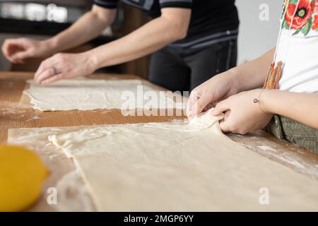 Mutter und Tochter haben den Teig auf den Küchentisch gestreut, um ihn weiter zu backen Stockfoto