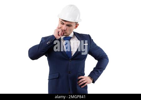 Ein gutaussehender Mann in Anzug und Helm, der sich Gedanken macht, ein Problem zu lösen, Hand am Kinn. Konzept im Studio auf weißem Hintergrund. Stockfoto