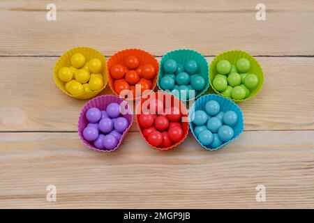 Die bunten Kugeln sind in einem Korb derselben Farbe angeordnet. Ein Spiel für die Entwicklung von Kindern. Auf einem Holzhintergrund Stockfoto