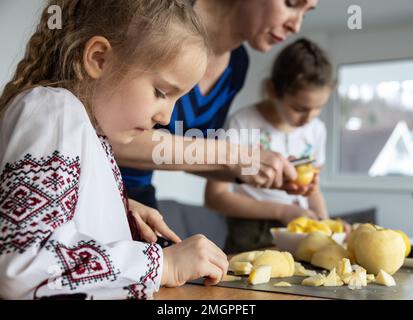 Eine Mutter und 2 Töchter schneiden Äpfel in kleine Stücke, vorne ein Mädchen in einem ukrainischen Hemd mit Stickerei Stockfoto