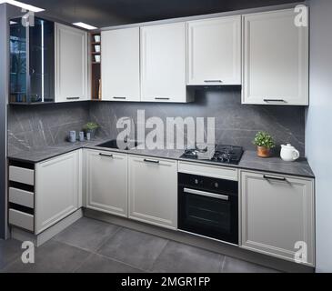 Innenausstattung der weiß-grauen Küche, horizontale, lineare Anordnung. Luxuriöse, modern ausgestattete Küche in flachem Design mit Glaselementen. Stockfoto