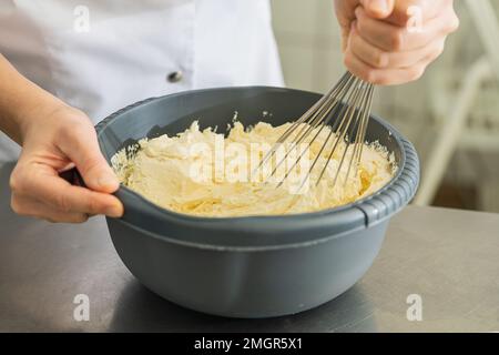 bäckerin hält Schüssel mit Teig und Schneebesen, um die umrührende Butter für einen Kuchen zu schlagen Stockfoto