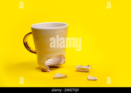 Zerbrochene Teetasse auf gelbem Hintergrund isoliert. Zerbrochene Kaffeetasse und zerbrechliche Keramikstücke Stockfoto