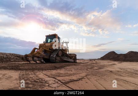 Der gelbe Bulldozer steht auf dem Boden. Vor dem Hintergrund des Sonnenuntergangs. Stockfoto