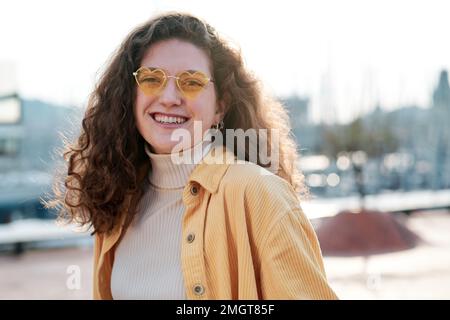 Eine Frau mit Sonnenbrille, die in die Kamera schaut und lächelt, während sie draußen posiert. Stockfoto