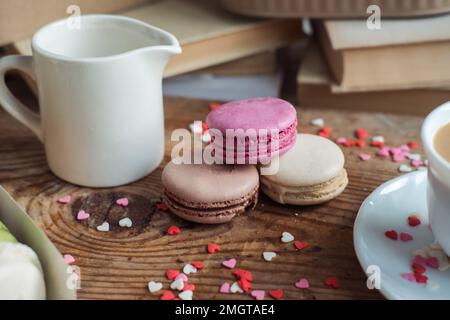 Makronen und eine Tasse Kaffee, ein Milchkännchen auf einem Hintergrund mit kleinen Herzen auf einem hölzernen Hintergrund, Draufsicht Stockfoto