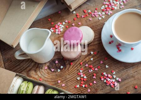 Makronen und eine Tasse Kaffee, ein Milchkännchen auf einem Hintergrund mit kleinen Herzen auf einem hölzernen Hintergrund, Draufsicht Stockfoto