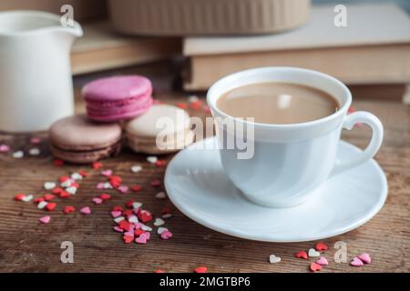 Makronen und eine Tasse Kaffee, ein Milchkännchen auf einem Hintergrund mit kleinen Herzen auf einem hölzernen Hintergrund, Draufsicht Stockfoto