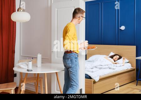 Ein Mann bringt seiner schlafenden Frau Frühstück ins Bett Stockfoto