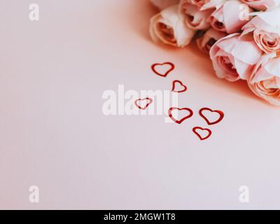 Rosafarbener, blühender Ranunculus auf pinkfarbenem festlichem Hintergrund, pastellfarbene Blumenkarte und Herzkonfetti. Alles gute zum Valentinstag, zum Muttertag, zum Geburtstag Stockfoto