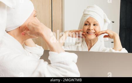 Seniorin mit einem Handtuch um den Kopf gewickelt, während sie ihre Morgenroutine im Badezimmer genießt Stockfoto