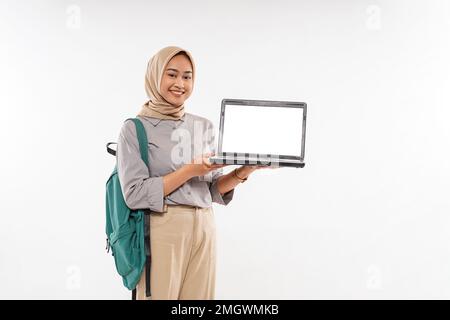 Eine schöne Schülerin mit Hidschab steht und zeigt den geöffneten Laptop Stockfoto