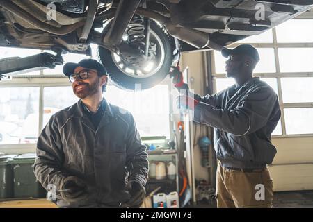 Geschulte Mechaniker, die in einer Autowerkstatt Autoreifen auf einem Aufzug prüfen. Hochwertige Fotos Stockfoto