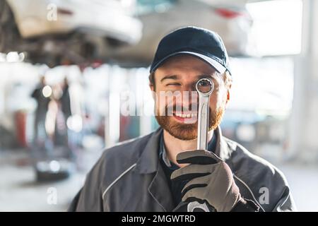 Ein komisches Porträt eines Automechanikers, der einen Metallschlüssel nahe an sein Auge hält. Hochwertige Fotos Stockfoto