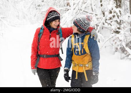 Mutter und Sohn haben Spaß beim Wandern im Winter während des Schneefalls in den Urwäldern der Region Notranjska, Dolenjske toplice, Slowenien Stockfoto